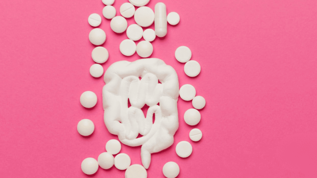 Representação artística do intestino feita com algodão e comprimidos sobre fundo rosa, simbolizando a saúde intestinal e o uso de medicamentos.